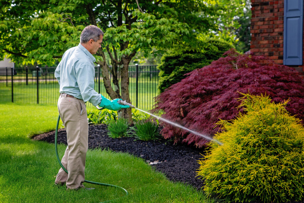 Technician applying tick control to landscape bed.